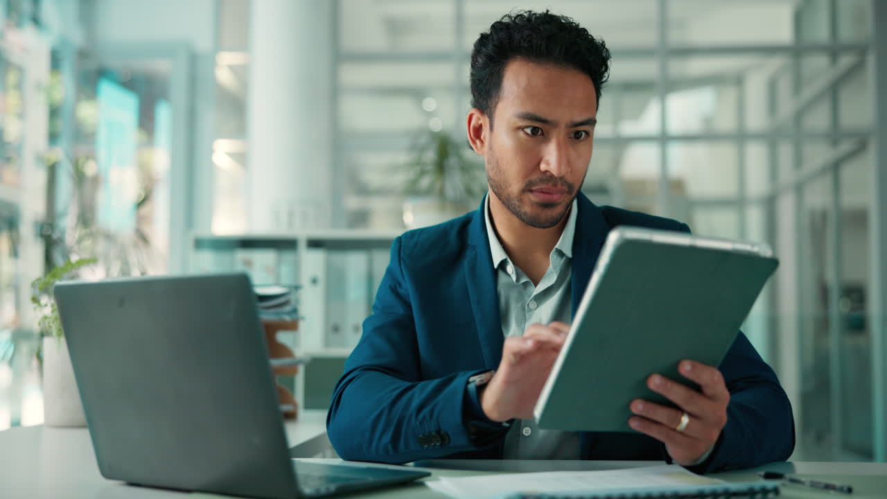 Uomo d'affari concentrato che lavora al laptop e al tablet in un ufficio moderno