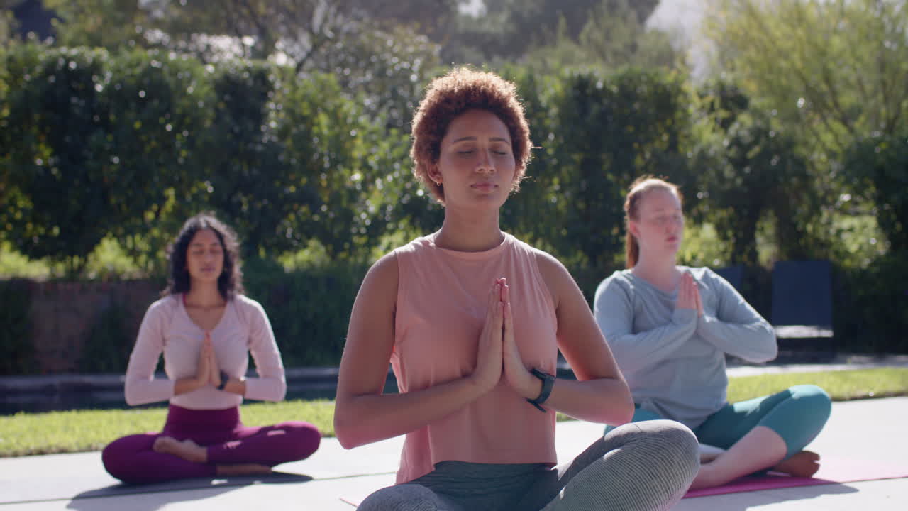Practicing yoga, diverse women meditating outdoors on yoga mats, relaxing together