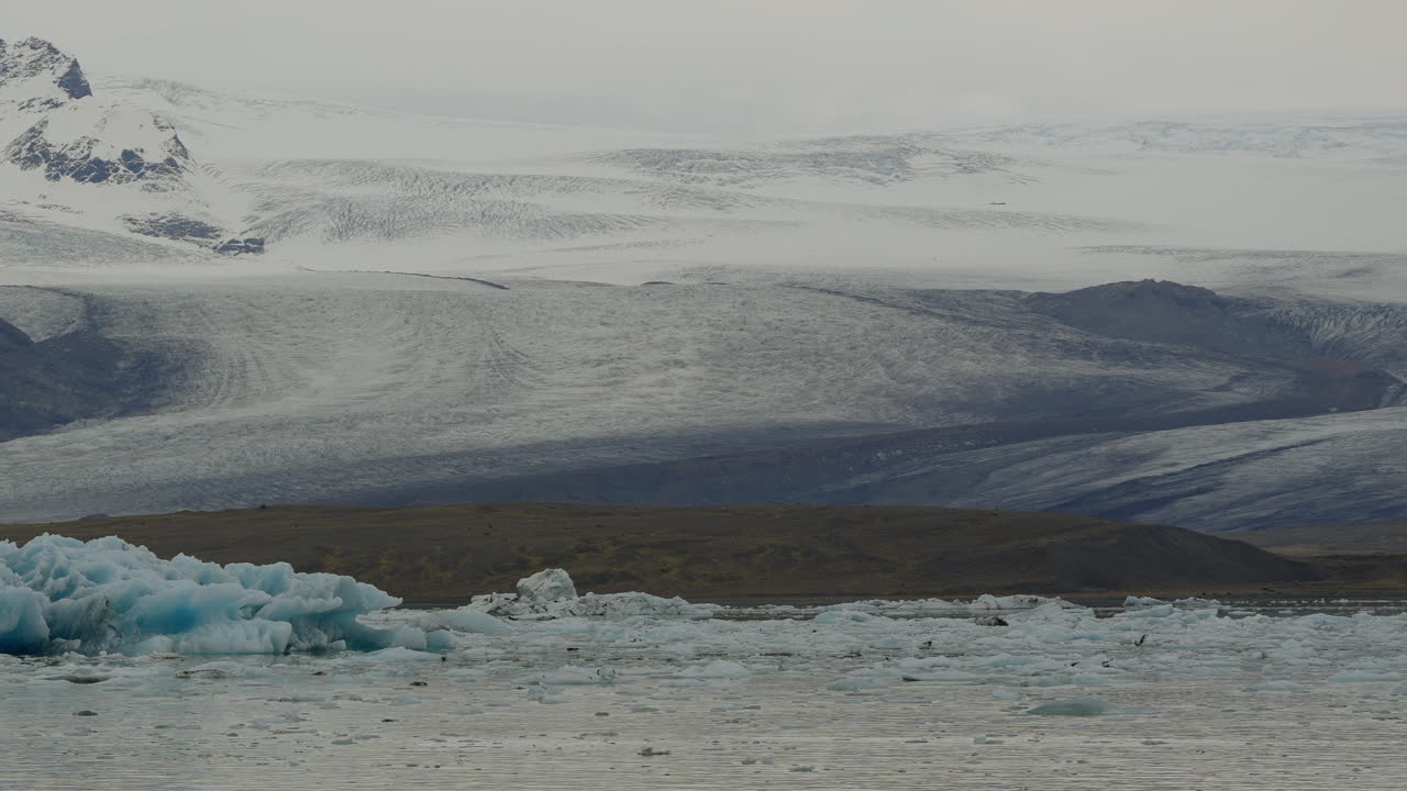 아이슬란드의 jökulsárlón에 있는 빙하 호수, 빙하가 얼어붙은 물 속에서 떠다니며, 배경에는 눈 인 산들이 있습니다.