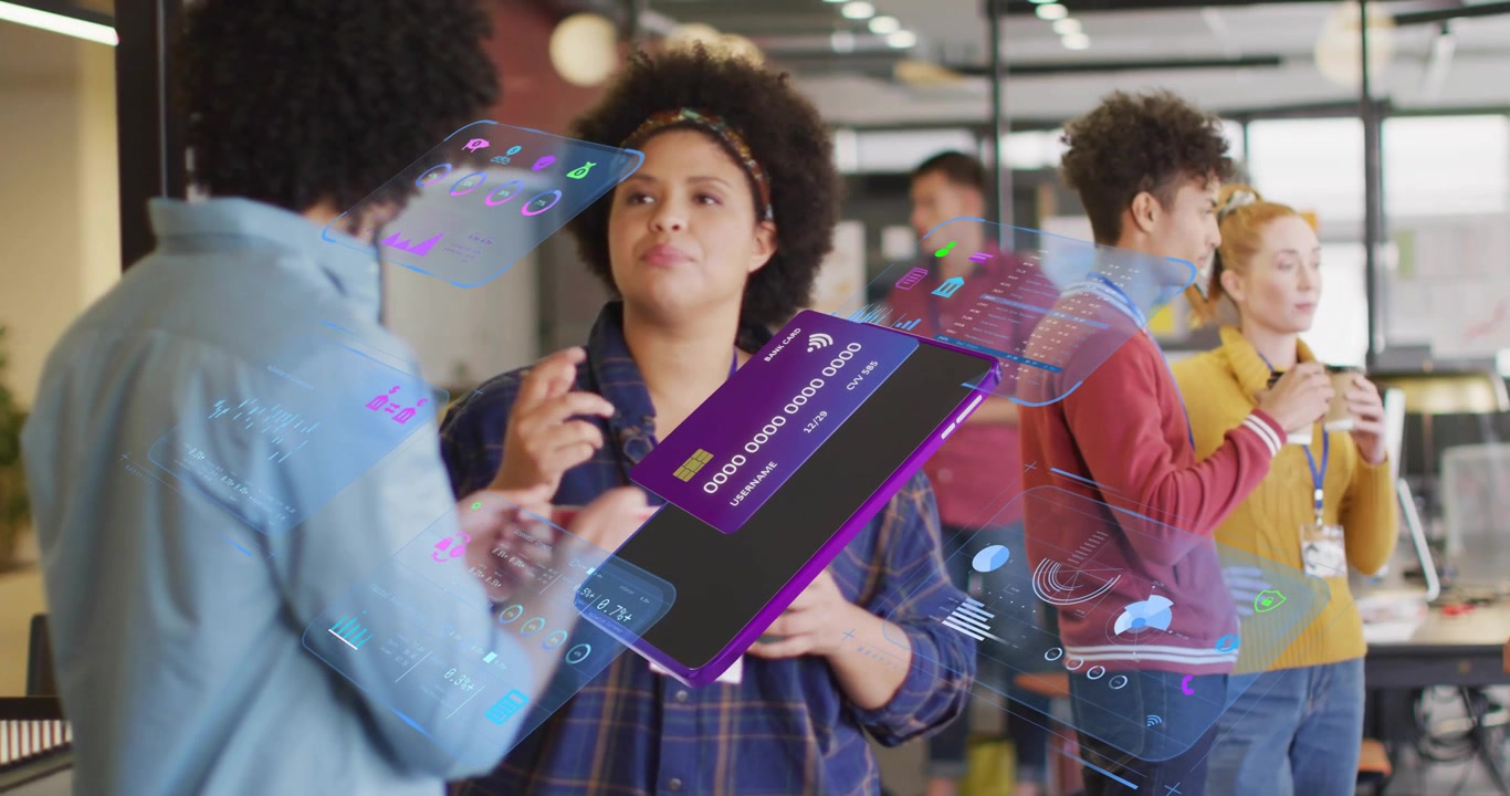 Mid adult woman pivoting device to colleague in tech discussion showing holographic UI icons charts