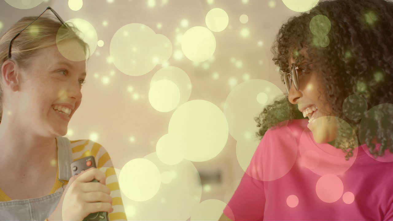 animación de puntos de luz sobre dos adolescentes felices y diversas imitando el canto con el control remoto de la tv