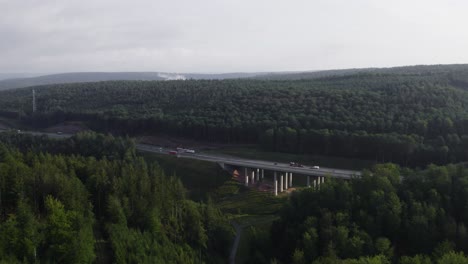 drone flying forwards through some trees in a german forest revealing a motorway where multiple vehicles are crossing it. concepts of roads and industrial constructions.