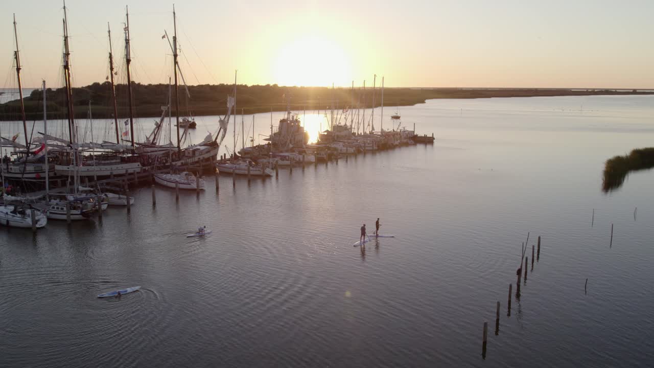 Aerial view of people supping on IJsselmeer at sunset in Makkum, Netherlands with stunning sunset lighting, calm atmosphere, high quality drone footage highlighting natural beauty