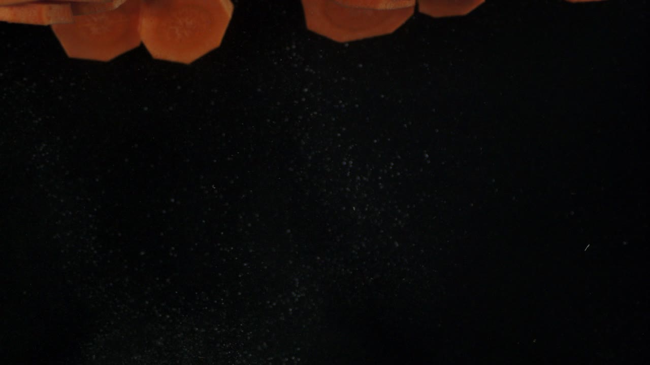 caer pedazos de zanahoria fresca en el agua con burbujas de aire.