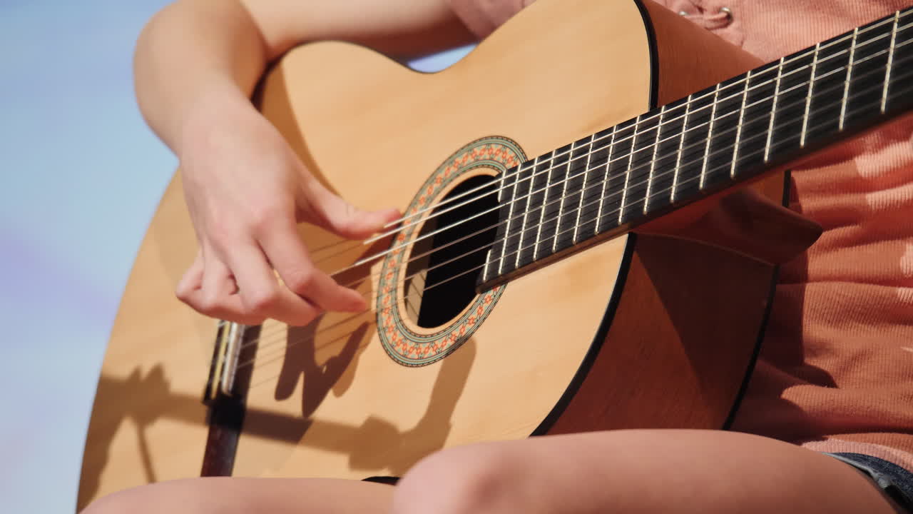 Talented female musician playing chords on a classical acoustic guitar during a sunny day
