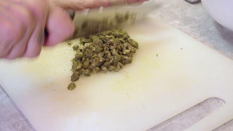 closeup view: woman chops capers, white chopping block with big knife
