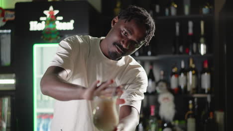 bartender adding straw to cocktail glass, finishing drink preparation in bar. behind, illuminated heineken neon sign and well-stocked bar shelves, creating a lively bar atmosphere