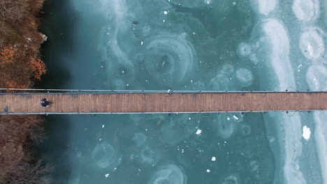 aerial: a man on crutches crosses a wooden bridge over a frozen lake