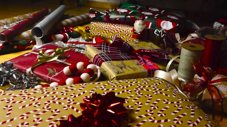 Footage panning over nicely wrapped Christmas presents and gifts with colorful wrapping paper and candy canes that are on a wooden floor under a Christmas tree. Wrapping paper rolls in the background.