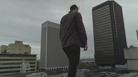 caucasian man walking along a rooftop in a city during a cloudy day