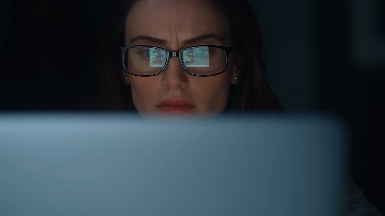 Donna caucasica concentrata sul bagliore del monitor, analista di dati remota a tarda notte che lavora contro una scadenza, occhiali riflettenti