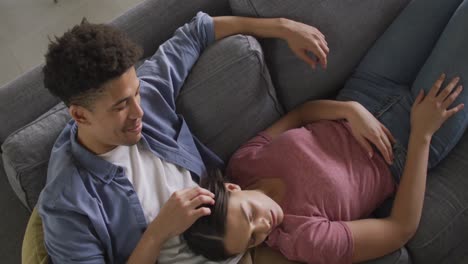 Happy-biracial-couple-sitting-on-sofa-in-living-room-embracing