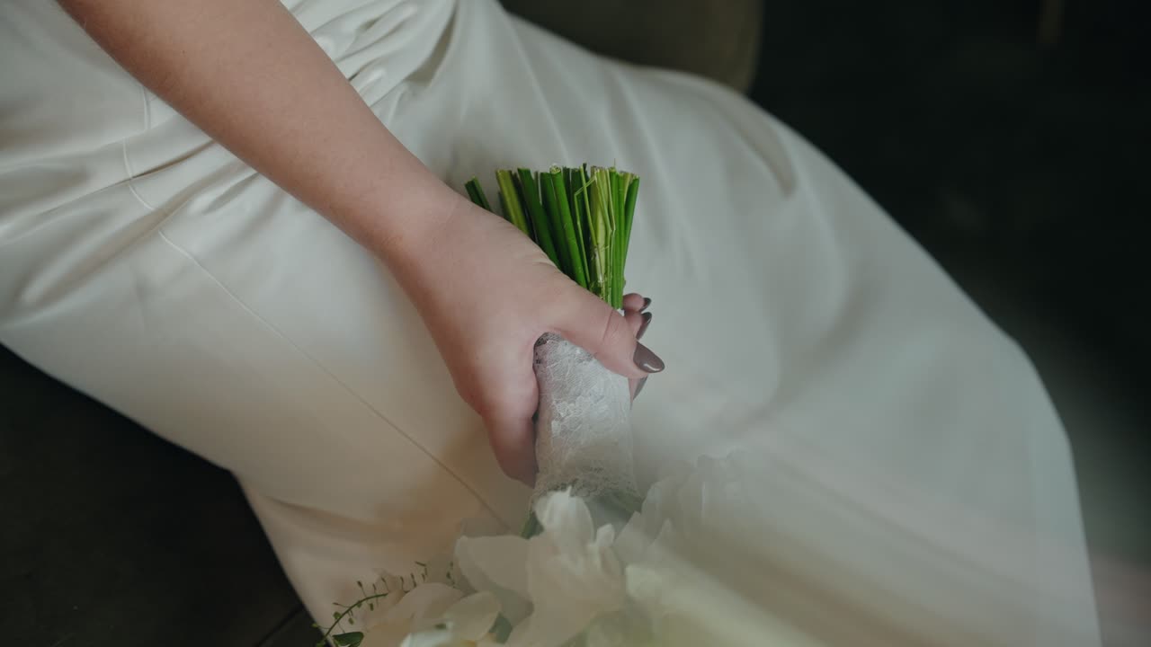Closeup of bride hand holding white bouquet indoor
