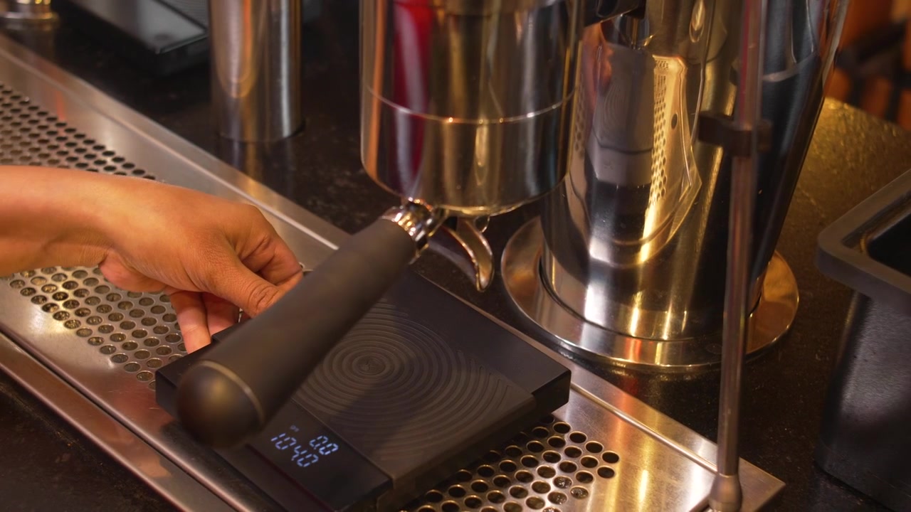 Bidikan aksi barista yang sedang menyiapkan seduhan espresso dengan memasang portafilter ke mesin profesional.