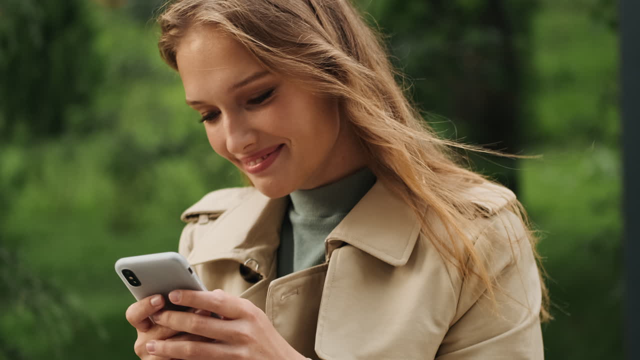 Happy Caucasian female student using smartphone outdoors.
