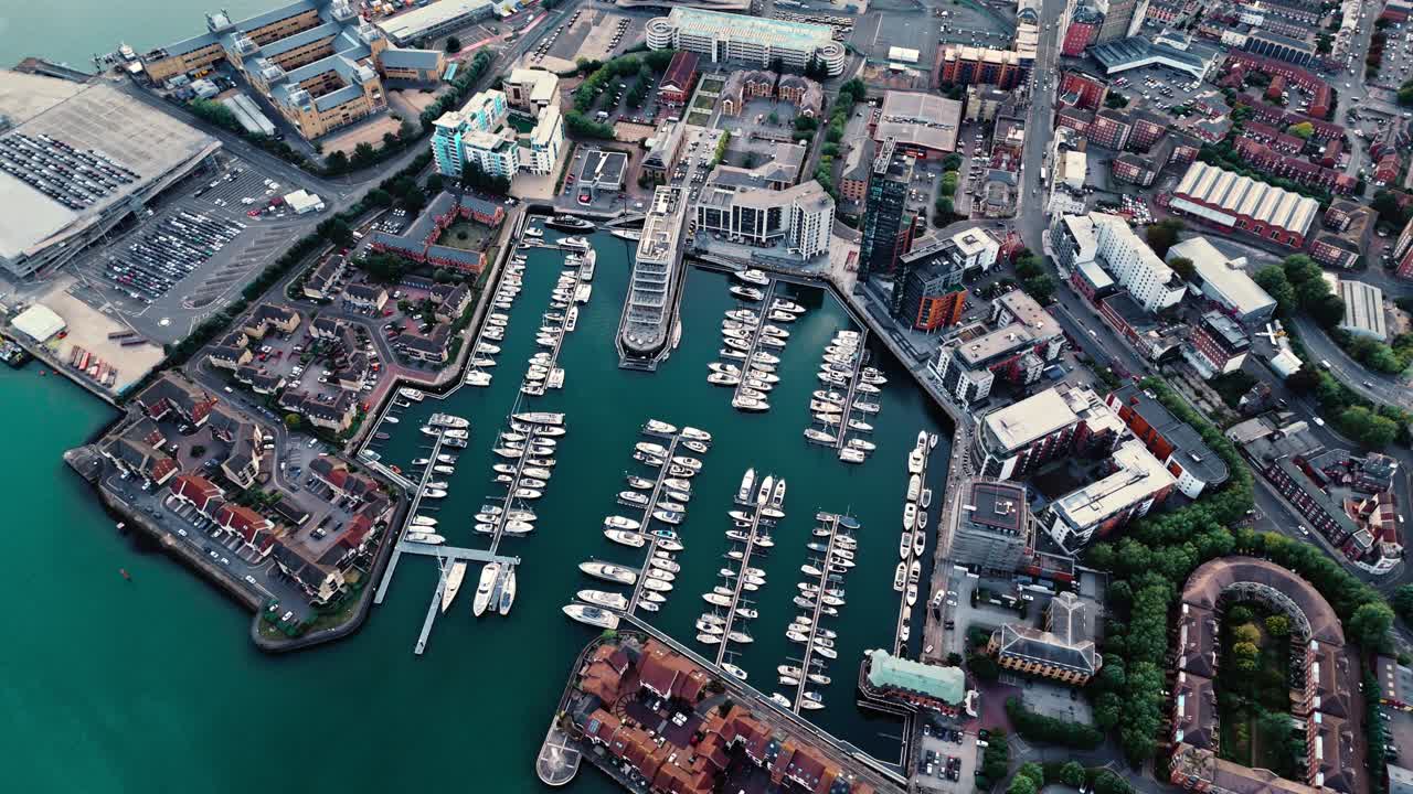Birds-eye aerial drone pans left over Ocean Village Southampton marina, capturing boats, calm waters, and autumn sunset colors glowing across the docks