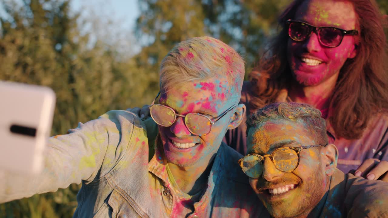 Uomini multietnici che posano per la fotocamera dello smartphone, scattano selfie e si divertono alla celebrazione Holi.