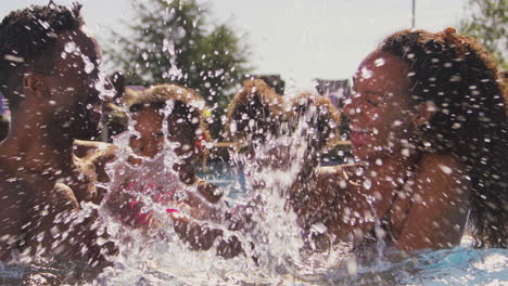 family on summer holiday with two girls being held in swimming pool by parents and splashing