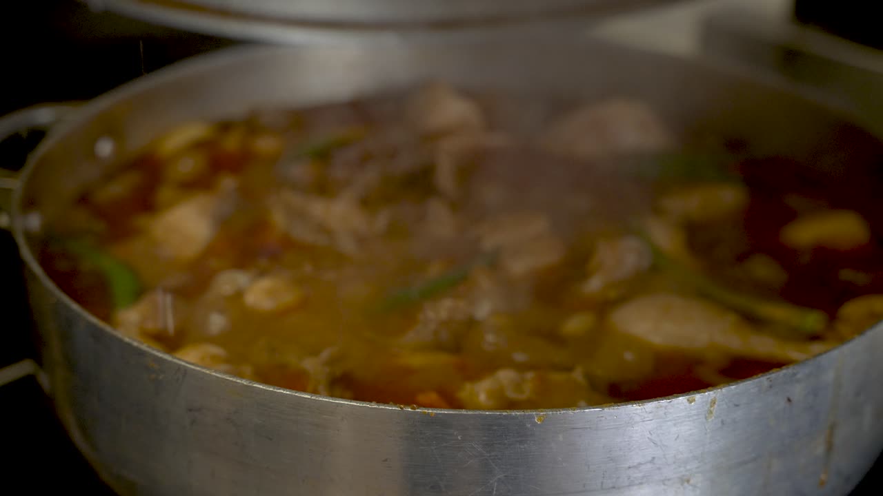 se levanta la tapa de una olla grande y se escapa el vapor del pollo al curry hirviendo a fuego lento