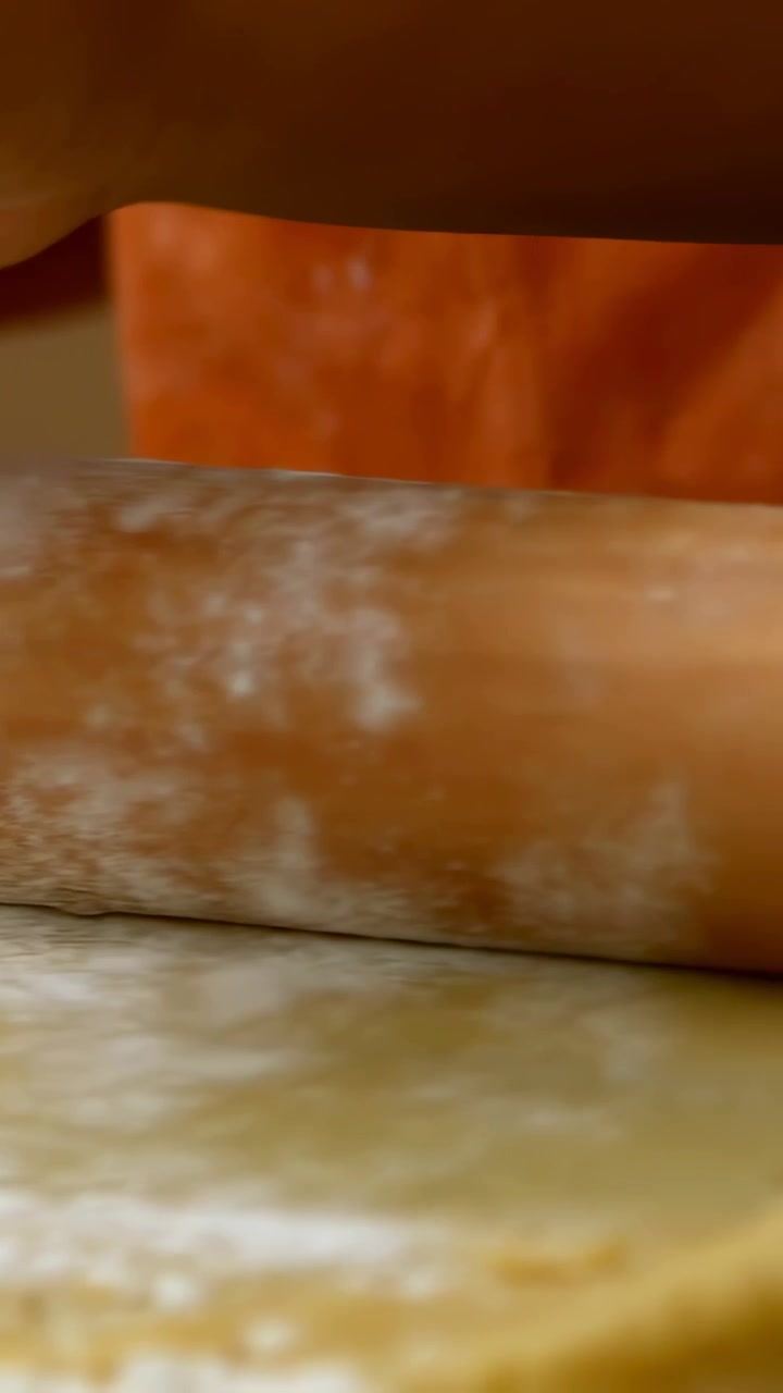 Vertical video: Rolling pin entering, cook rolling dough for baking at counter, orange apron