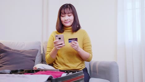 beautiful asian woman booking flight online with her cell phone and credit card for travel in the summertime