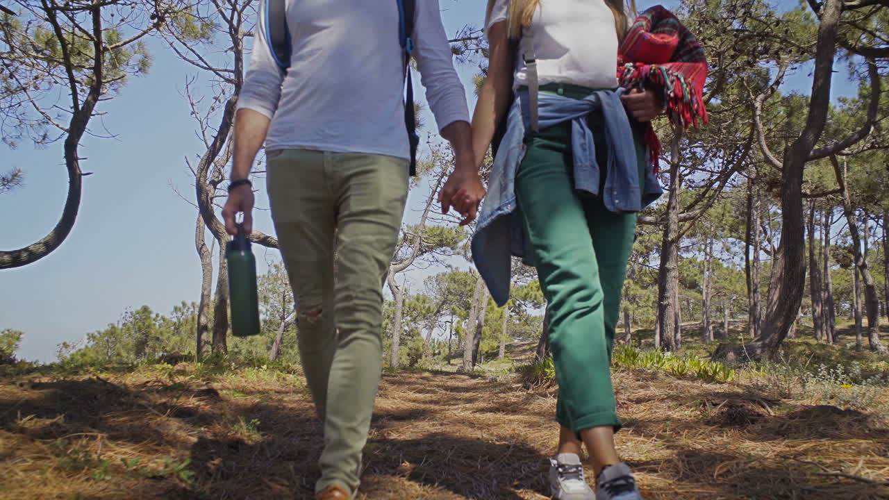 sección baja de una pareja con mochilas caminando por el bosque