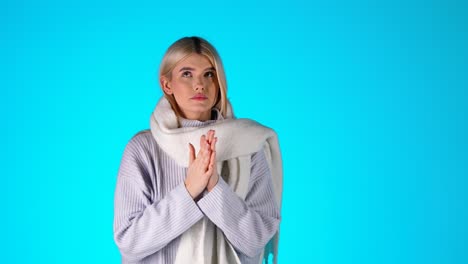 young blonde woman feeling cold, shivering, blowing and rubs hands to warm up, colorful studio shot