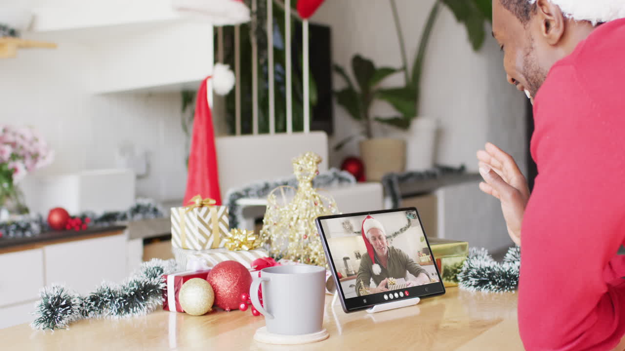 hombre afroamericano con sombrero de santa teniendo llamada de video de tableta con hombre caucásico feliz