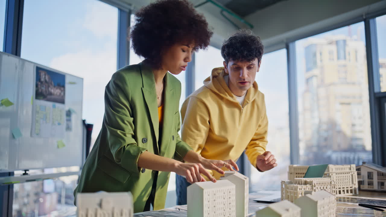Construction engineers discussing models of residential buildings in office