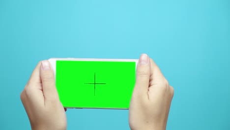 woman using smart phone with green screen on blue table background. female hands scrolling pages, tapping on touch screen.