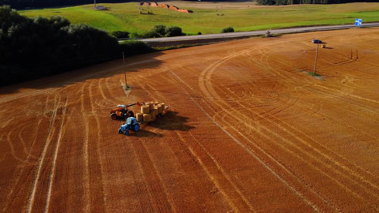una vista aérea de un gran campo dorado industrial con un tractor recogiendo pacas de heno