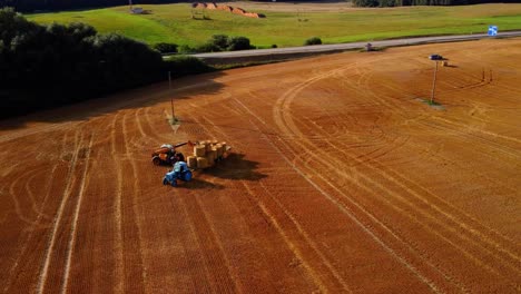 Eine-Luftaufnahme-Eines-Großen-Industriellen-Goldenen-Feldes-Mit-Einem-Traktor,-Der-Heuballen-Sammelt