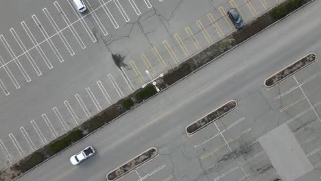 static birds eye view of a parking lot and mall access road with traffic passing and lot light poles visible