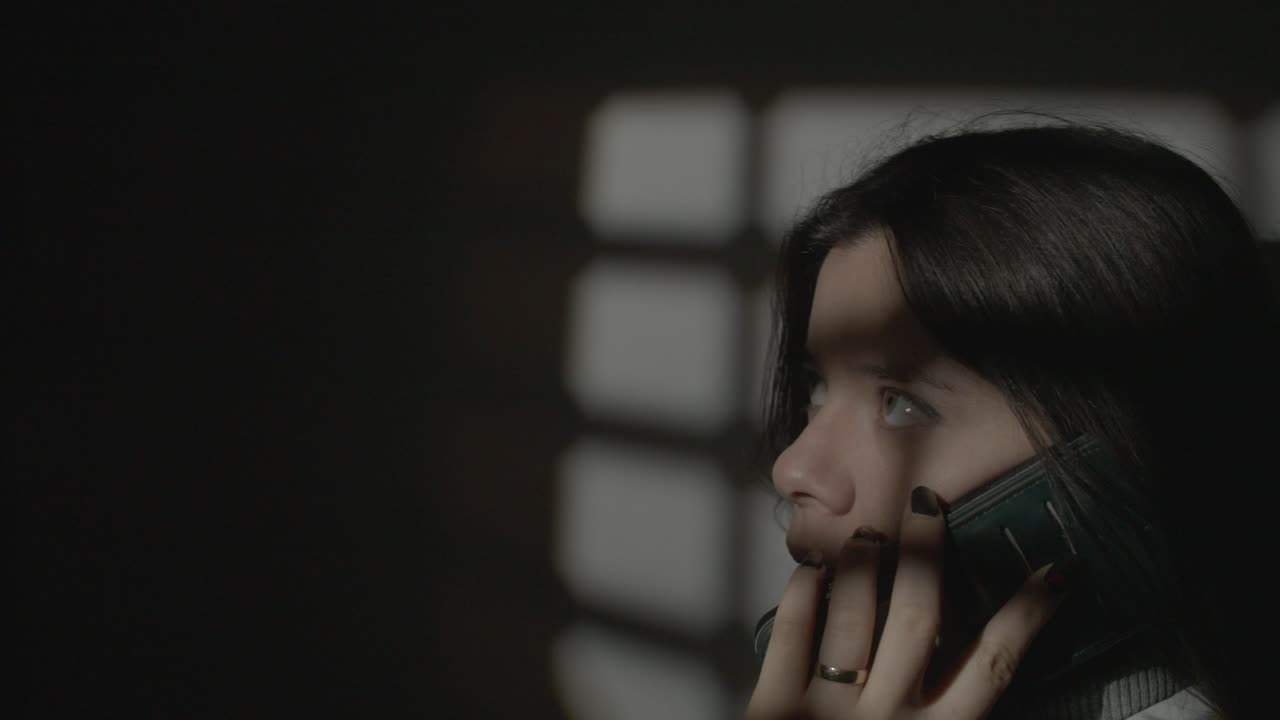 Woman making phone call indoors with artistic shadow and light patterns from a window