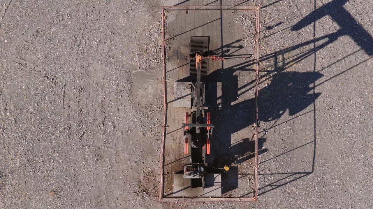 Static drone view from above shows an oil pumpjack enclosed in fencing with a distinct shadow over the gravel desert of Vaca Muerta, in Patagonia, Argentina