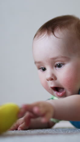 active baby waving hands lying on the floor. caucasian child trying to reach a toy in front of him. light backdrop in blur. vertical video
