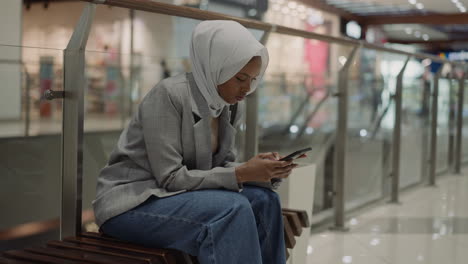 muslim black woman chats on phone in shopping center hall