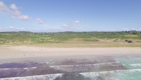 Aerial-flyback-over-Goulien-beach-and-surfers-in-Brittany,-France