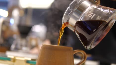 Ein-Mann-Nimmt-Eine-Glaskaraffe-Mit-Kaffee-Im-Unscharfen-Vordergrund-Und-Gießt-Sie-In-Eine-Gelbe-Tasse,-Gießt-Schwarzen-Kaffee-In-Eine-Tasse-Aus-Einer-Kaffeekanne