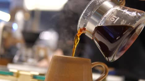 a man takes a glass carafe containing coffee in the blurred foreground and pours it into a yellow cup, pour black coffee into a mug from a coffee pot