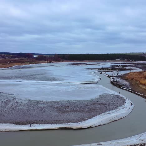 Environmental problems. Frozen river on a dirty background of nature. Gloomy atmosphere of spring landscape