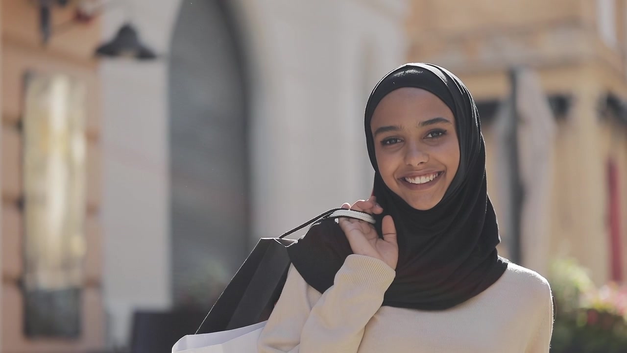 Giovane donna sorridente con hijab e borse della spesa all'aperto