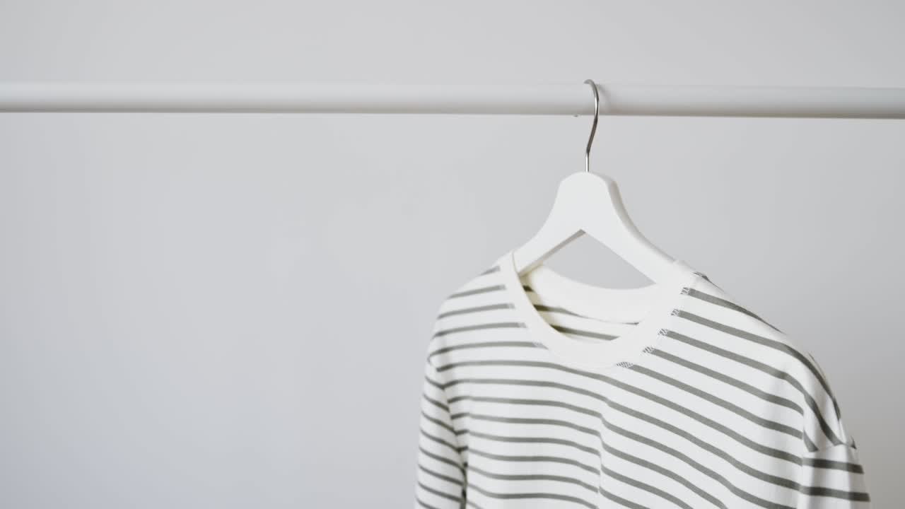 chaqueta de moda de moda para mujeres, manga larga, sudadera a rayas en colgante de madera blanco cuelga en el estante contra la pared blanca. concepto de ropa minimalista, publicidad de la tienda, venta, descuentos, compras