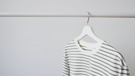 women's fashion trendy jacket, longsleeve, striped sweatshirt on white wooden hanger hangs on rack against white wall. minimalistic clothing concept, store advertising, sale, discounts, shopping