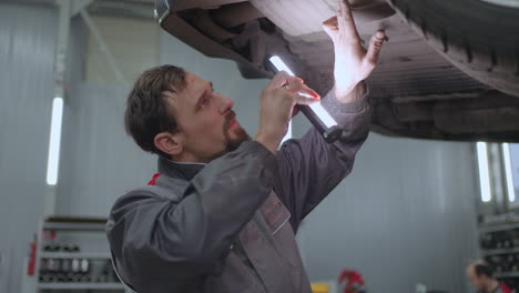 man auto mechanic looks under the car raised on the lift in search of malfunctions in slow motion