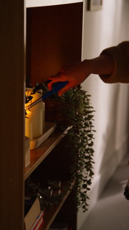 vertical video close up of woman at home using electronic lighter to light candles on shelf in lounge