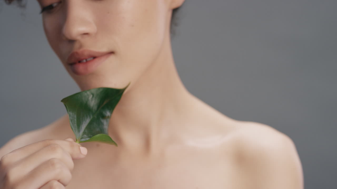 가까운 초상화 섹시한 젊은 여성이 잎으로 몸을 만지며 부드러운 건강한 피부 피부색을 즐기며 회색 배경의 자연스러운 아름다움을 즐기고 피부 관리 개념