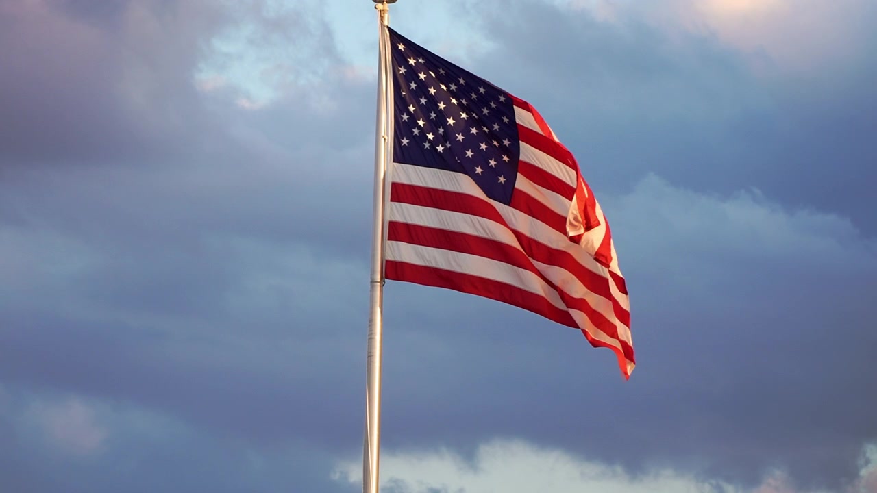 Amerikansk flag vajende stolt mod en blød solopgangshimmel i Clermont, Florida, med varmt morgenlys der oplyser stjernerne og striberne
