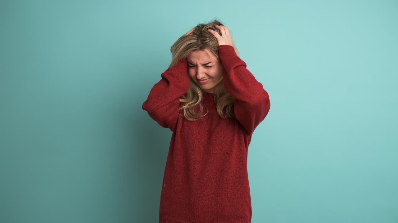 Frustrated woman suffering from headache in blue studio