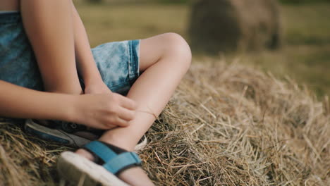 close-up of child hands playing with hay while sitting on hay bale in sunlit rural field, soft blurred background adds depth, creating a peaceful and nostalgic countryside